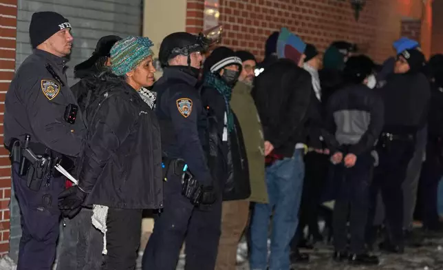 Protesters in cuffs wait to be loaded into a bus after staging a sit-in at the lobby of a Hilton Garden Inn in New York, Tuesday, Jan. 27, 2026. (AP Photo/Seth Wenig)