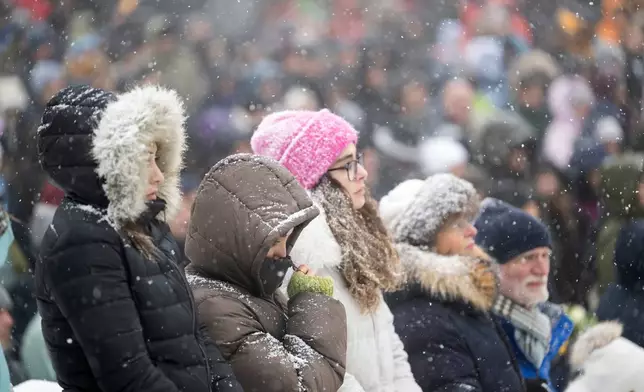 People gather to watch the official commemorative ceremony on a giant screen in front of the St. Christopher Chapel in Crans-Montana during the national day of mourning following the deadly fire at the "Le Constellation" bar in Crans-Montana, Switzerland, Friday, Jan. 9, 2026. (Alessandro della Valle/Keystone via AP)
