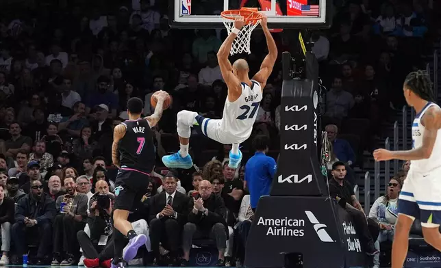 Minnesota Timberwolves center Rudy Gobert (27) swings on the basket after dunking past Miami Heat center Kel'el Ware (7) during the first half of an NBA basketball game, Saturday, Jan. 3, 2026, in Miami. (AP Photo/Rebecca Blackwell)