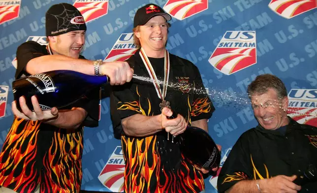 FILE - U.S. skier Bode Miller, left, sprays sparkling wine on Phil McNichol, head coach of the U.S. men's alpine ski team, as Daron Rahlves, center, smiles during a victory party in the American House in Bormio, Italy, Feb. 5, 2005. (AP Photo/Thomas Kienzle, File)