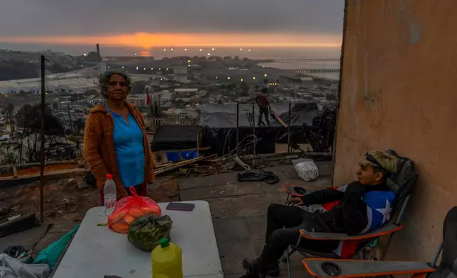 Residents Alicia Roa and grandson Jonathan Escalona rest on the roof of their house that was damaged by wildfires in Lirquen, Chile, Tuesday, Jan. 20, 2026. (AP Photo/Javier Torres)