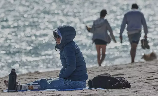 A bundled up Lucia Amato, of Argentina, sits on the shore while waiting for a friend in Miami Beach, Fla., Thursday, Jan. 29, 2026.A bundled up (AP Photo/Marta Lavandier)