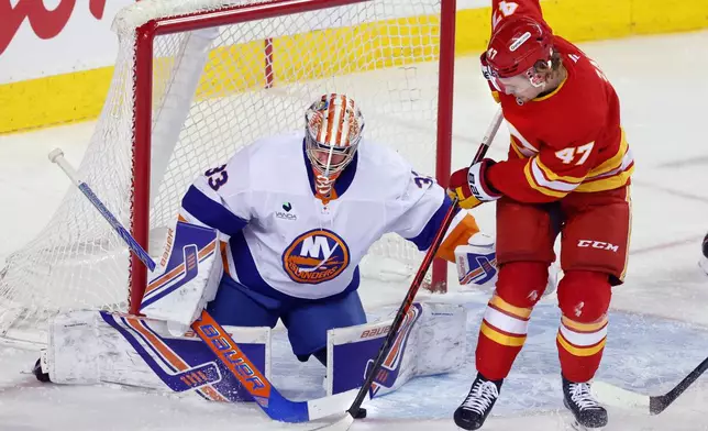 New York Islanders goalie David Rittich, left, makes a save against Calgary Flames' Connor Zary during the first period of an NHL hockey game in Calgary, Alta., Saturday, Jan. 17, 2026. (Larry MacDougal /The Canadian Press via AP)