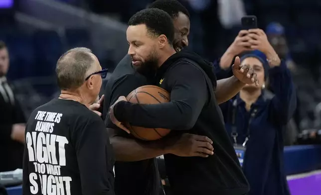 Golden State Warriors guard Stephen Curry, foreground middle, hugs Miami Heat forward Andrew Wiggins before an NBA basketball game in San Francisco, Monday, Jan. 19, 2026. (AP Photo/Jeff Chiu)