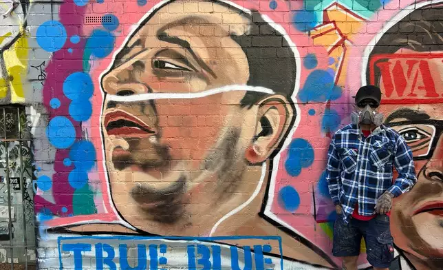 Street artist Jarrod Grech poses for a photo next to his painting of Ahmed al Ahmed, a 43-year-old Syrian-Australian shopkeeper who disarmed one of the attackers of Sydney's Bondi Beach shooting, in Melbourne, Australia, Sunday, Dec. 28, 2025. (Rod McGuirk/AP Photo)