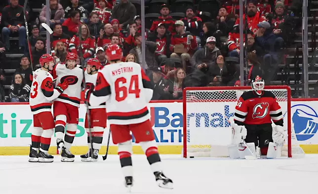 New Jersey Devils goaltender Jake Allen (34) looks on while Carolina Hurricanes left wing Taylor Hall, second from left, celebrates after his goal with teammates in the second period of an NHL hockey game, Sunday, Jan. 4, 2026, in Newark, N.J. (AP Photo/Heather Khalifa)