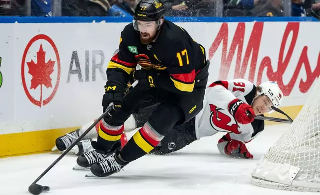 Vancouver Canucks' Filip Hronek (17) skates with the puck as New Jersey Devils' Arseny Gritsyuk (81) slides into the boards during the second period of an NHL hockey game in Vancouver, British Columbia, Friday, Jan. 23, 2026. (Ethan Cairns/The Canadian Press via AP)