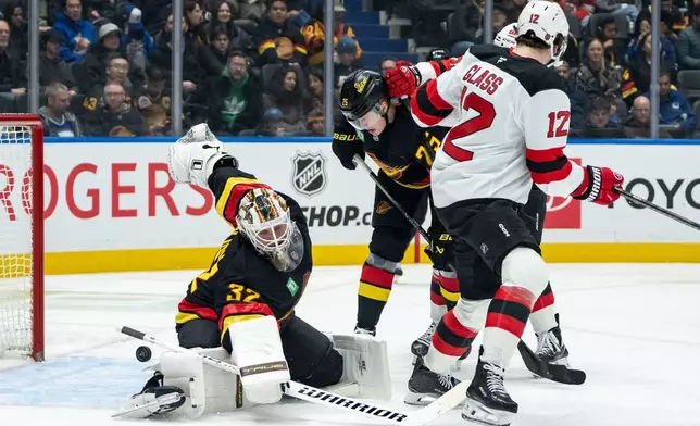 New Jersey Devils' Cody Glass (12) scores against Vancouver Canucks goaltender Kevin Lankinen (32) as Canucks' Elias Pettersson (25) watches during the second period of an NHL hockey game in Vancouver, British Columbia, Friday, Jan. 23, 2026. (Ethan Cairns/The Canadian Press via AP)