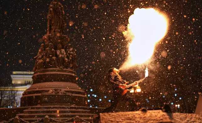FILE - A street performer spits fire and plays a guitar in the snow in St. Petersburg, Russia, Dec. 29, 2025. (AP Photo/Dmitri Lovetsky, File)