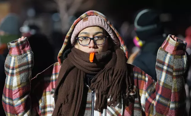 A person holds a whistle in their mouth as police face off with protesters during a noise demonstration outside the Graduate by Hilton Minneapolis hotel on Wednesday, Jan. 28, 2026, in Minneapolis. (AP Photo/Adam Gray)