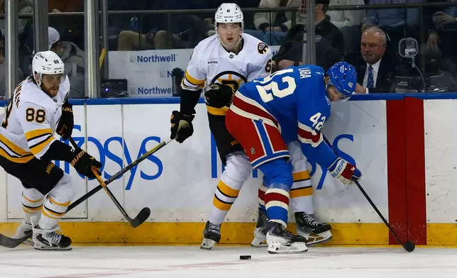 Boston Bruins forward David Pastrnak, left, and defenseman Mason Lohrei, center, battle along the boards with New York Rangers center Noah Laba, right, during the second period of an NHL hockey game Monday, Jan. 26, 2026, in New York. (AP Photo/John Munson)