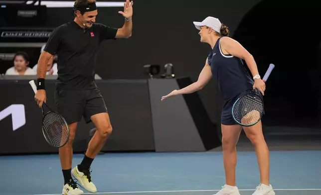 Roger Federer of Switzerland reacts with partner Ash Barty of Australia in their doubles match against Lleyton Hewitt and Pat Rafter of Australia during the Opening Ceremony for the Australian Open tennis championship in Melbourne, Australia, Saturday, Jan. 17, 2026. (AP Photo/Dita Alangkara)