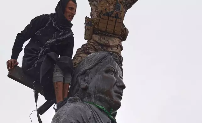 FILE - Syrian government soldiers wave a Syrian flag after climbing atop a statue of a female Kurdish fighter, following the takeover of the town from U.S.-backed Syrian Democratic Forces (SDF) during an ongoing push against Kurdish-led forces, in Tabqa, eastern Syria, Jan. 18, 2026. (AP Photo/Omar Albam, File)