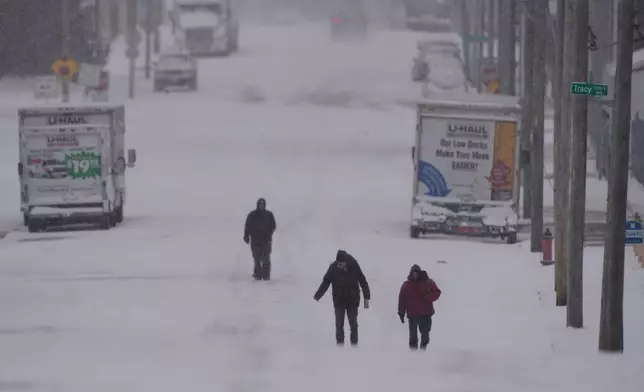 People walk on a snow-covered street as a winter storm passes though the area Saturday, Jan. 24, 2026, in Kansas City, Mo. (AP Photo/Charlie Riedel)