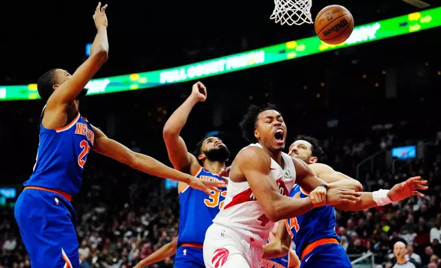 Toronto Raptors' Scottie Barnes (4) is fouled by New York Knicks' Landry Shamet (right) as Knicks' Mikal Bridges (left) and Karl-Anthony Towns (32) defend during first half NBA basketball action in Toronto on Wednesday, Jan. 28, 2026. (Frank Gunn/The Canadian Press via AP)