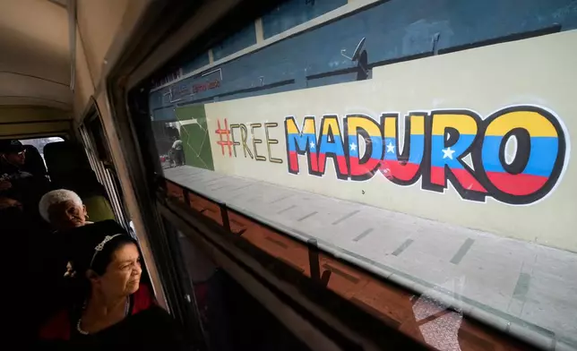 Commuters ride a bus past a mural calling for the release of former Venezuelan President Nicolas Maduro, who was detained by U.S. forces, in Caracas, Venezuela, Thursday, Jan. 8, 2026. (AP Photo/Matias Delacroix)