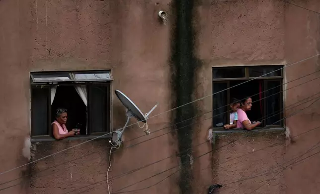 Residents watch firefighters and civil defense workers at the site of a landslide caused by heavy rains and severe flooding in the Parque Burnier neighborhood of Juiz de Fora in Minas Gerais state, Brazil, Tuesday, Feb. 24, 2026. (AP Photo/Silvia Izquierdo)
