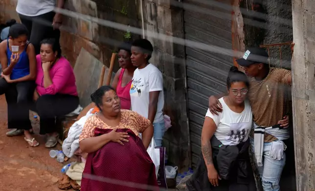 Residents watch as firefighters and civil defense workers at the site where homes collapsed due to heavy rains and severe flooding in the Parque Burnier neighborhood of Juiz de Fora in Minas Gerais state, Brazil, Tuesday, Feb. 24, 2026. (AP Photo/Silvia Izquierdo)