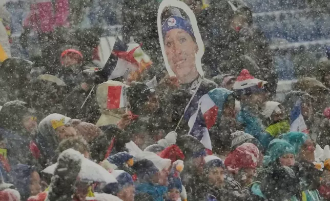 French fans hold a photo of Oceane Michelon of France the Biathlon Women's 12.5km Mass Start at the 2026 Winter Olympics, in Anterselva, Italy, Saturday, Feb. 21, 2026. (AP Photo/Christophe Ena)