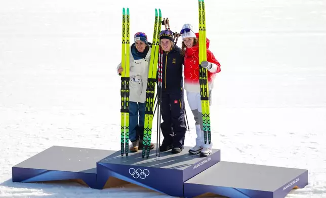 Gold medalist Ebba Andersson, of Sweden, poses on the podium flanked by silver medalist Heidi Weng, of Norway, left, and bronze medalist Nadja Kaelin, of Switzerland, after the cross country skiing women's 50km mass start classic at the 2026 Winter Olympics, in Tesero, Italy, Sunday, Feb. 22, 2026. (AP Photo/Kirsty Wigglesworth)