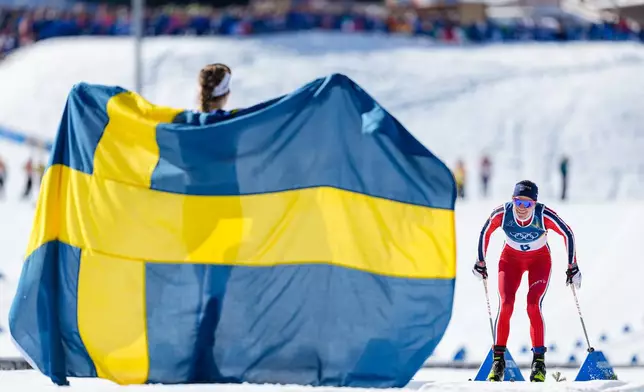 Gold medalist Ebba Andersson, of Sweden, left, watches Heidi Weng, of Norway, approach the finish line to win the silver medal in the cross country skiing women's 50km mass start classic at the 2026 Winter Olympics, in Tesero, Italy, Sunday, Feb. 22, 2026. (AP Photo/Matthias Schrader)