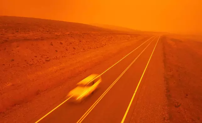 A car speeds along a road as smoke from wildfires turns the sky red near Cholila, Argentina, Sunday, Feb. 1, 2026. (AP Photo/Victor R. Caivano)