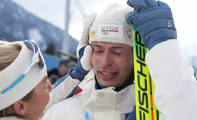 ADDS NAME OF TEAMMATE - Sturla Holm Laegreid, of Norway, reacts after he won bronze as teammate Ingrid Landmark Tandrevold comforts him after the men's 20-kilometer individual biathlon race at the 2026 Winter Olympics in Anterselva, Italy, Tuesday, Feb. 10, 2026. (AP Photo/Andrew Medichini)