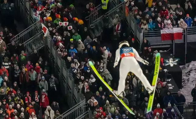 Fans watch Nozomi Maruyama, of Japan, soaring through the air during the ski jumping mixed team competition at the 2026 Winter Olympics, in Predazzo, Italy, Tuesday, Feb. 10, 2026.(AP Photo/Evgeniy Maloletka)
