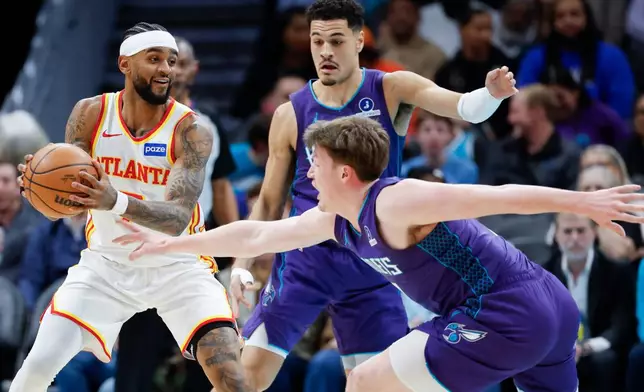 Atlanta Hawks guard Nickeil Alexander-Walker, left, looks to pass against Charlotte Hornets guards Kon Knueppel, right, and Josh Green during the first half of an NBA basketball game in Charlotte, N.C., Wednesday, Feb. 11, 2026. (AP Photo/Nell Redmond)