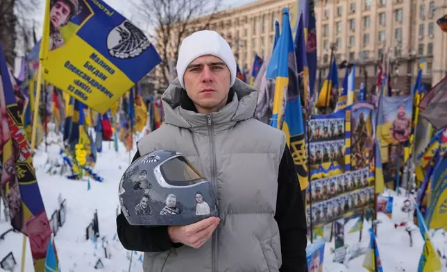 Ukrainian skeleton athlete Vladyslav Heraskevych holds his crash helmet as he stands outside an improvised memorial to fallen soldiers killed in Russia - Ukraine war at Independence square in Kyiv, Ukraine, Wednesday, Feb. 18, 2026. (AP Photo/Sergei Grits)