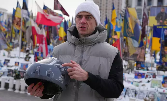 Ukrainian skeleton athlete Vladyslav Heraskevych holds his crash helmet as he stands outside an improvised memorial to fallen soldiers killed in Russia - Ukraine war at Independence square in Kyiv, Ukraine, Wednesday, Feb. 18, 2026. (AP Photo/Sergei Grits)