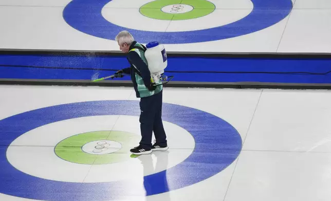 A staff member sprays water on the ice before the bronze medal curling mixed doubles match at the 2026 Winter Olympics, in Cortina d'Ampezzo, Italy, Tuesday, Feb. 10, 2026. (AP Photo/Misper Apawu)