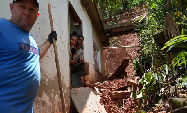 Vilma Goncalves da Silva, center left, and her son Samuel Goncalves, look out from their front door the damage caused by flooding near the affected areas where homes collapsed in the Parque Burnier neighborhood of Juiz de Fora, in Minas Gerais state, Brazil, Wednesday, Feb. 25, 2026. (AP Photo/Silvia Izquierdo)