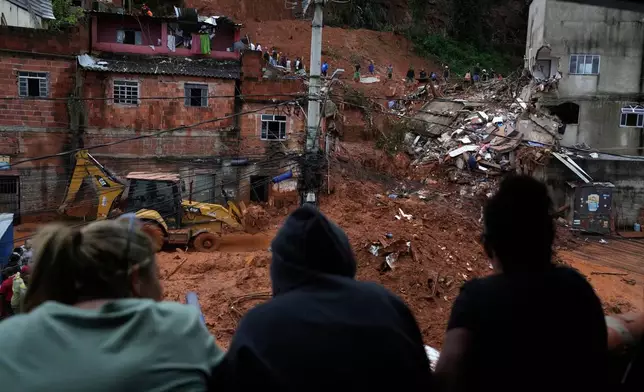 Residents watch firefighters and civil defense workers at the site where homes collapsed due to heavy rains and severe flooding in the Parque Burnier neighborhood of Juiz de Fora in Minas Gerais state, Brazil, Tuesday, Feb. 24, 2026. (AP Photo/Silvia Izquierdo)