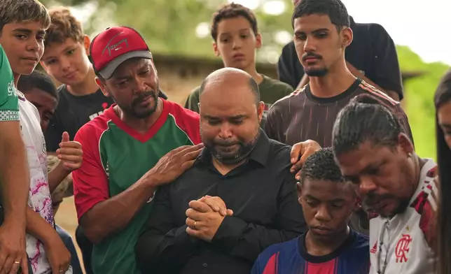 Ricardo Dutra, center, the father of 11-year-old Bernardo Lopes, a victim of heavy rains and flooding, is comforted by his son's friends during the burial of his child in Juiz de Fora, Minas Gerais state, Brazil Wednesday, Feb. 25, 2026. (AP Photo/Silvia Izquierdo)