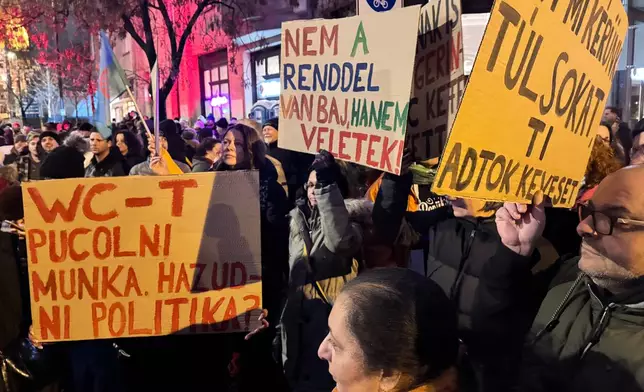 Demonstrators hold signs, one reading, at left, reading "Cleaning toilets is work but lying is politics?" at a protest against a Hungarian government minister called over comments he made about the Roma minority, in Budapest, Hungary, Saturday, Jan. 31, 2026. (AP Photo/Bela Szandelszky)