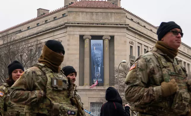 Members of the National Guard walk past a banner with President Donald Trump hanging on the Department of Justice, Thursday, Feb. 19, 2026, in Washington. (AP Photo/Allison Robbert)