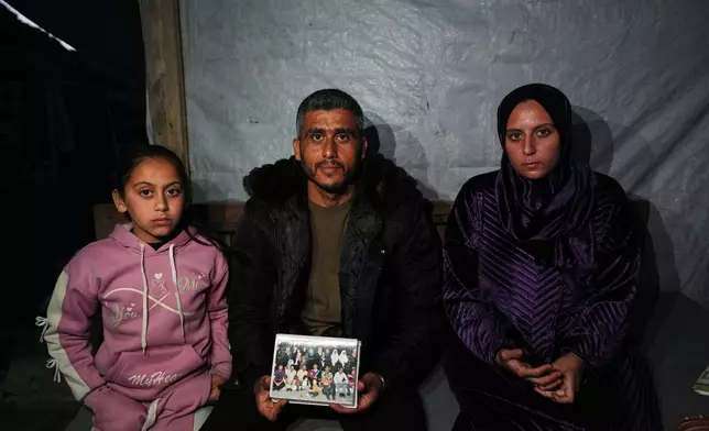 Saddam al-Yazji, center, poses for a portrait with his wife, Heba, and their daughter, Maryam, while holding a picture of their extended family in Gaza City Tuesday, Feb. 24, 2026. (AP Photo/Jehad Alshrafi)