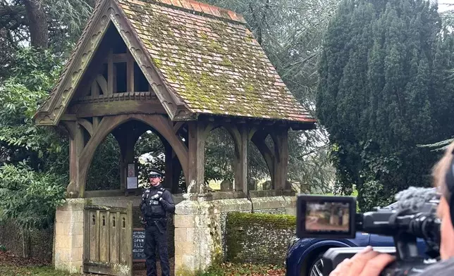 A camera man films a police officer guarding the entrance to Churchyard of the Sandringham Royal Estate in Sandringham, Thursday, Feb. 19, 2026 after Andrew Mountbatten-Windsor has been arrested by British police on suspicion of misconduct in public office. (AP Photo/Matthew Kemp)