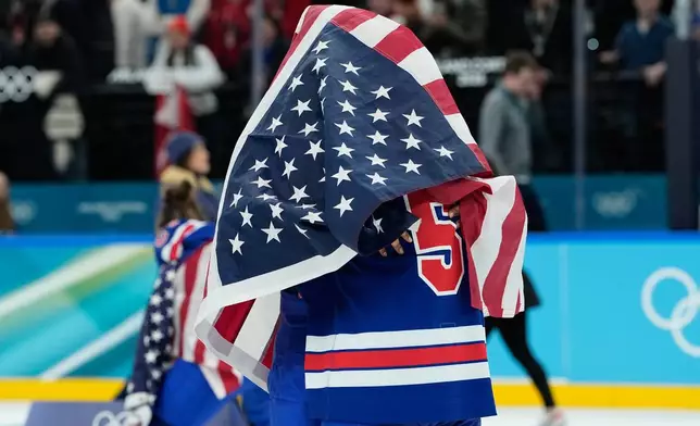 United States' Megan Keller (5), covered in the U.S. flag, gets a hug from a teammate after the United States' women's ice hockey team stand after being presented with the gold medals at the 2026 Winter Olympics, in Milan, Italy, Thursday, Feb. 19, 2026. (AP Photo/Petr David Josek)