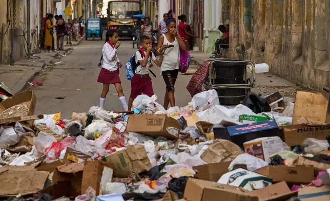 People hold their noses as they pass a street with garbage in Havana, Tuesday, Feb. 17, 2026. (AP Photo/Ramon Espinosa)