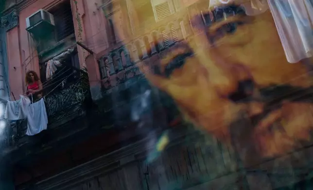 FILE - A Cuban woman hanging laundry on her balcony is seen reflected in a glass window decorated with a poster of Cuba's leader Fidel Castro in Old Havana, Cuba, Thursday, Dec. 27, 2007. (AP Photo/Dado Galdieri, File)