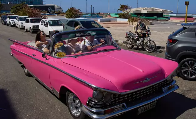 Tourists travel in a classic American car next to a line of drivers waiting to buy fuel for their cars in Havana, Cuba, Monday, Feb. 16, 2026. (AP Photo/Ramon Espinosa)