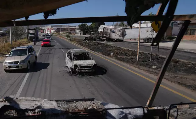 Vehicles pass a burned car a day after the Mexican army killed the leader of the Jalisco New Generation Cartel, Nemesio Oseguera Cervantes, known as "El Mencho," in Guadalajara, Mexico, Monday, Feb. 23, 2026. (AP Photo/Marco Ugarte)