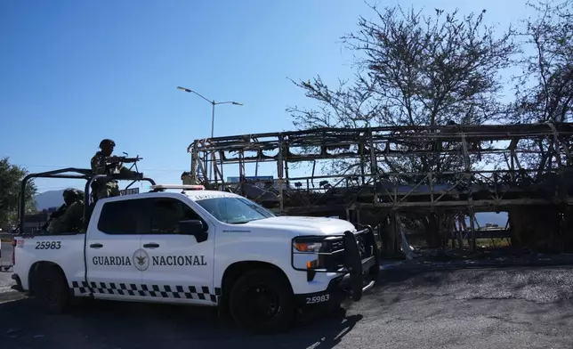 National Guard patrol past a charred vehicle the day after the Mexican army killed Jalisco New Generation Cartel leader Nemesio Oseguera Cervantes, known as "El Mencho," in Guadalajara, Mexico, Monday, Feb. 23, 2026. (AP Photo/Marco Ugarte)