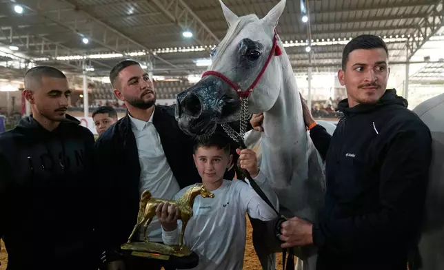 Owners and trainers pose for a photo with their horse Sultanat al-Tarab and her trophy, born in 2017 and a gold champion in her class, during the third and final day of the 18th Palestine Championship for Purebred Arabian Horses, in the West Bank city of Jericho, Saturday, Feb. 14, 2026. (AP Photo/Nasser Nasser)