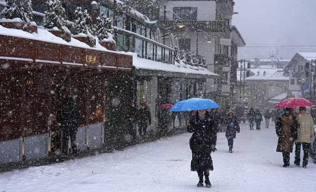 People walk along a main shopping street as snow falls ahead of the 2026 Winter Olympics, in Cortina d'Ampezzo, Italy, Tuesday, Feb. 3, 2026. (AP Photo/Fatima Shbair)