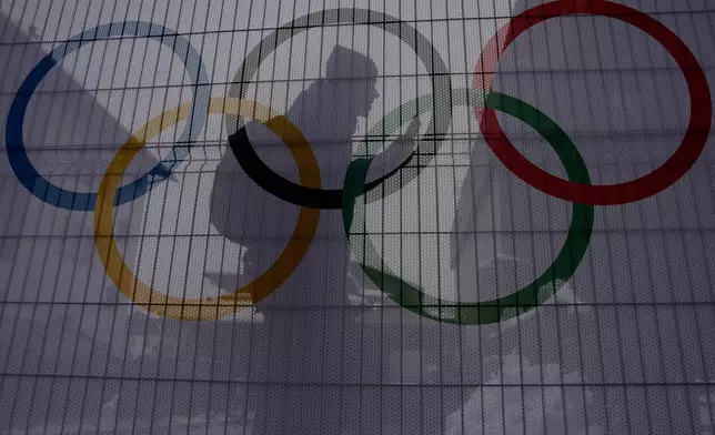 A person walks past Olympic rings on net covered fences at the 2026 Winter Olympics, in Bormio, Italy, Wednesday, Feb. 4, 2026. (AP Photo/John Locher)