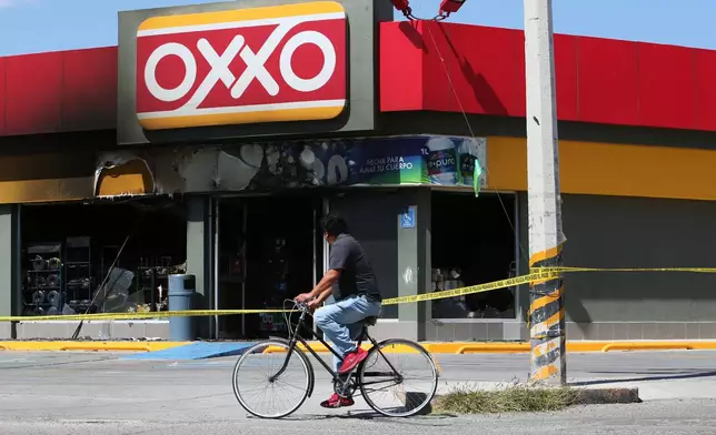 A man rides a bike next to a convenience store that was set on fire, in San Francisco del Ricon, Guanajuato state, Mexico, Sunday, Feb. 22, 2026, after the death of the leader of the Jalisco New Generation Cartel, Nemesio Ruben Oseguera Cervantes, known as "El Mencho." (AP Photo/Alfredo Valadez)