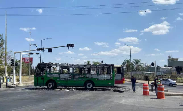 Pedestrians walk past charred buses that were set on fire, on a road in Guadalajara, Jalisco state, Mexico, Sunday, Feb. 22, 2026, after the death of the leader of the Jalisco New Generation Cartel, Nemesio Rubén Oseguera Cervantes, known as "El Mencho." (AP Photo/Refugio Ruiz)